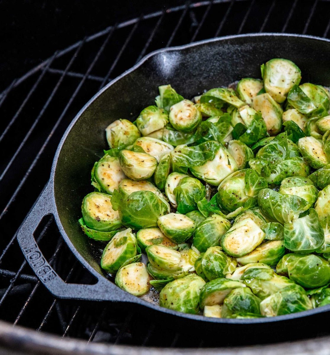 A cast iron skillet filled with halved Brussels sprouts, lightly seasoned, and cooking on a grill. The vibrant green sprouts are slightly browned on the edges, indicating they are being grilled to perfection.