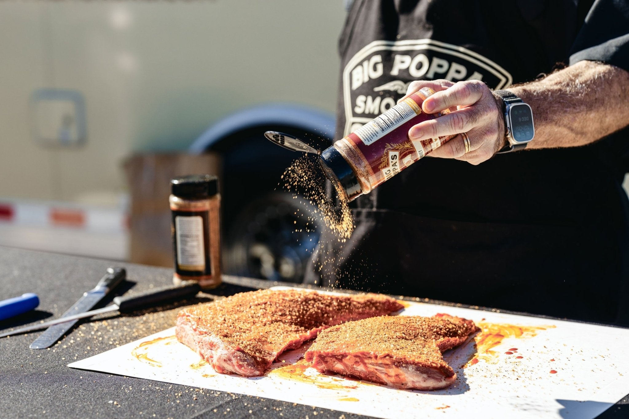 Big Poppa seasoning two tri-tips with a shaker of Big Poppa's Money Seasoning.