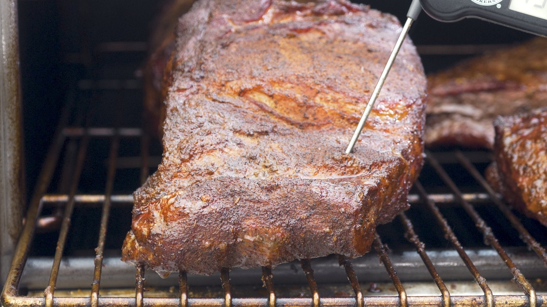 Picture of a pork butt with a nice brown crust with a probe going through it.