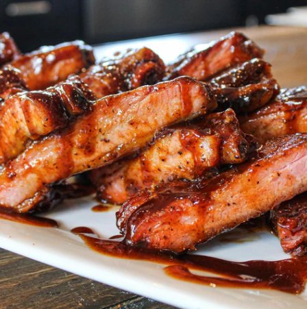 Plate of ribs glazed with Blues Hog Honey Mustard Sauce, showcasing a glistening golden coating. Ready to tantalize taste buds