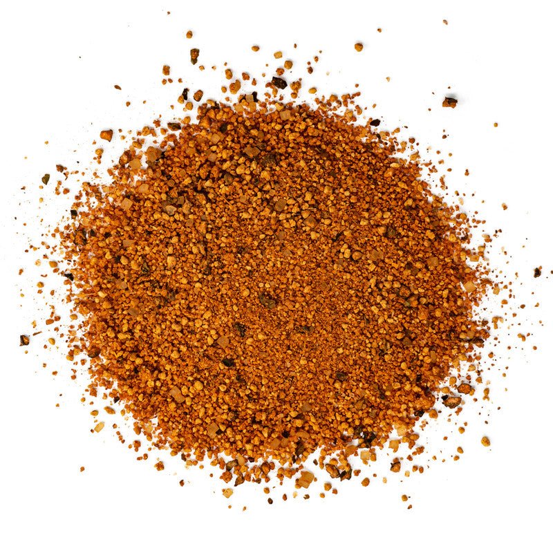 A close-up of Boars Night Out BBQ Rub seasoning spread out on a white surface. The seasoning is a coarse blend of reddish-brown particles, indicating a mix of spices and herbs typically used for barbecuing.