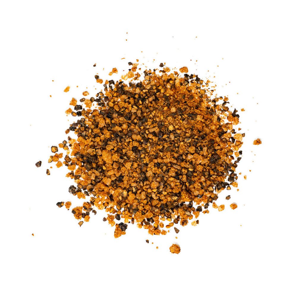 A close-up view of a pile of coarse seasoning blend, featuring black and orange-brown granules on a white background.