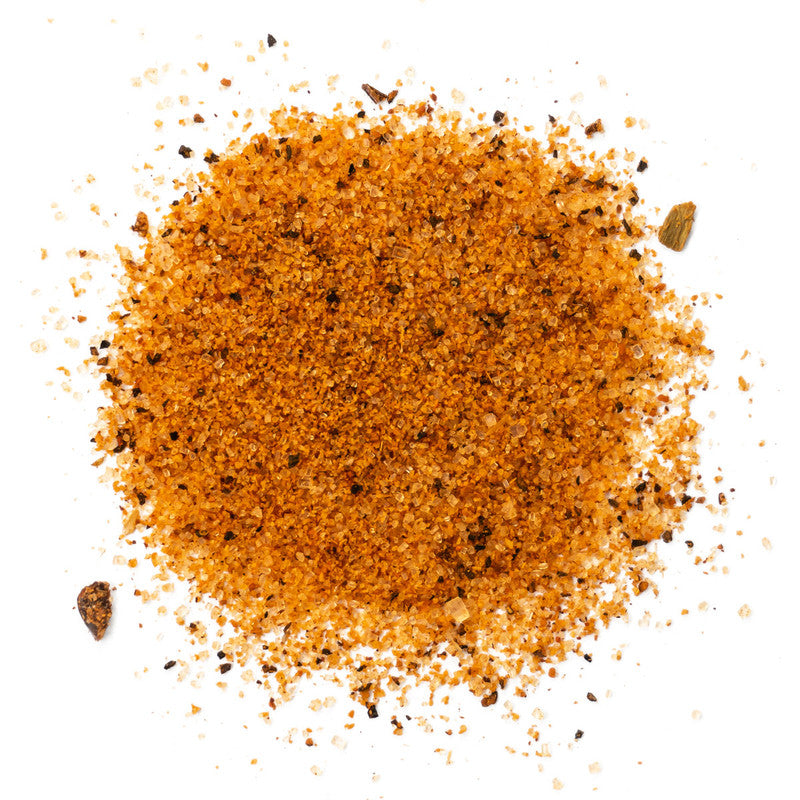A close-up of Cimarron Doc's Sweet Rib Rub & Bar-B-Q Seasoning spread out on a white surface. The seasoning is a coarse blend of reddish-brown particles with visible flecks of black, indicating a mix of spices and herbs.