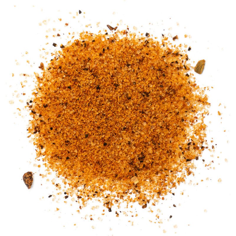 A close-up of Cimarron Doc's Sweet Rib Rub & Bar-B-Q Seasoning spread out on a white surface. The seasoning is a coarse blend of reddish-brown particles with visible flecks of black, indicating a mix of spices and herbs.