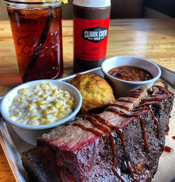 Clark Crew meal that features ribs, beans, cornbread, cheesy corn with ice tea and Clarks Crew BBQ Sauce