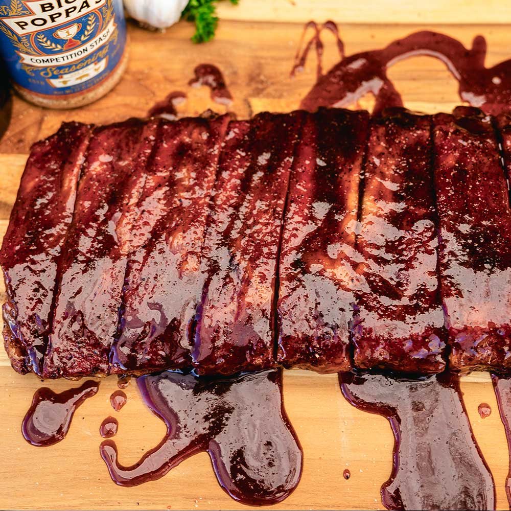 ribs sliced and presented on a wooden butcher block, drenched in mouthwatering barbecue sauce and seasoned well with bbq seasoning. competition stash is subtly displayed in the top left corner with some garnish peaking behind it