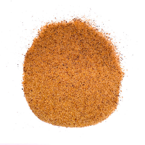 Close-up view of a pile of orange-brown seasoning powder, composed of granulated particles with visible flakes of spices and herbs, ideal for enhancing meat dishes.