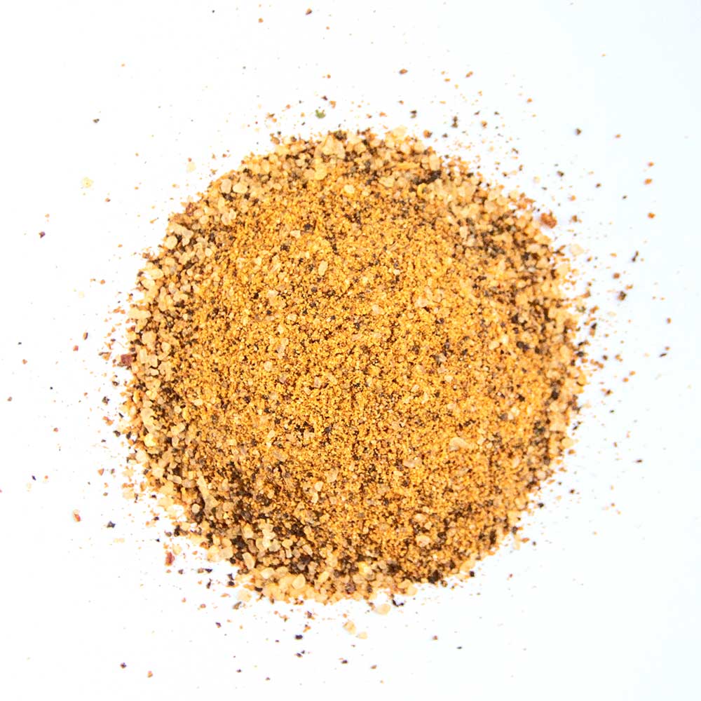 A pile of Big Poppa's Double Secret Seasoning on a white background, showing a mix of coarse and fine granules in various shades of brown and yellow.
