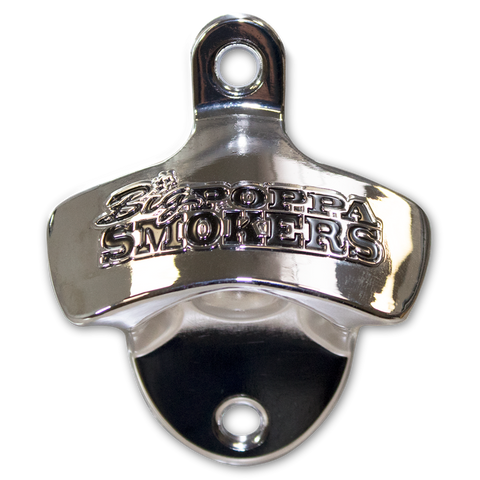 Close-up of a shiny stainless steel bottle opener embossed with the 'Big Poppa Smokers' logo. The opener has a classic top-pull design, featuring a curved handle with a circular hole for hanging and a black, concave base for cap removal, set against a black background.