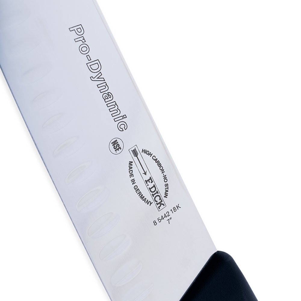 Close-up image of the F. Dick 7" Santoku Kullenschliff - ProDynamic. The knife features a high-carbon stainless steel blade with a kullenschliff edge to prevent food from sticking. It has a black ergonomic handle designed for comfort and control. Displayed on a plain white background, highlighting its sharpness and professional design.