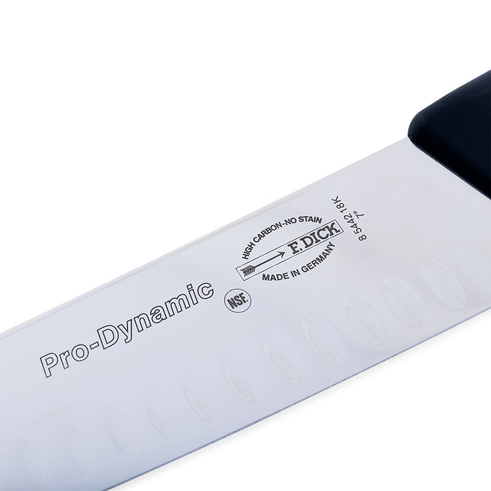 Close-up image of the F. Dick 7" Santoku Kullenschliff - ProDynamic. The knife features a high-carbon stainless steel blade with a kullenschliff edge to prevent food from sticking. It has a black ergonomic handle designed for comfort and control. Displayed on a plain white background, highlighting its sharpness and professional design.