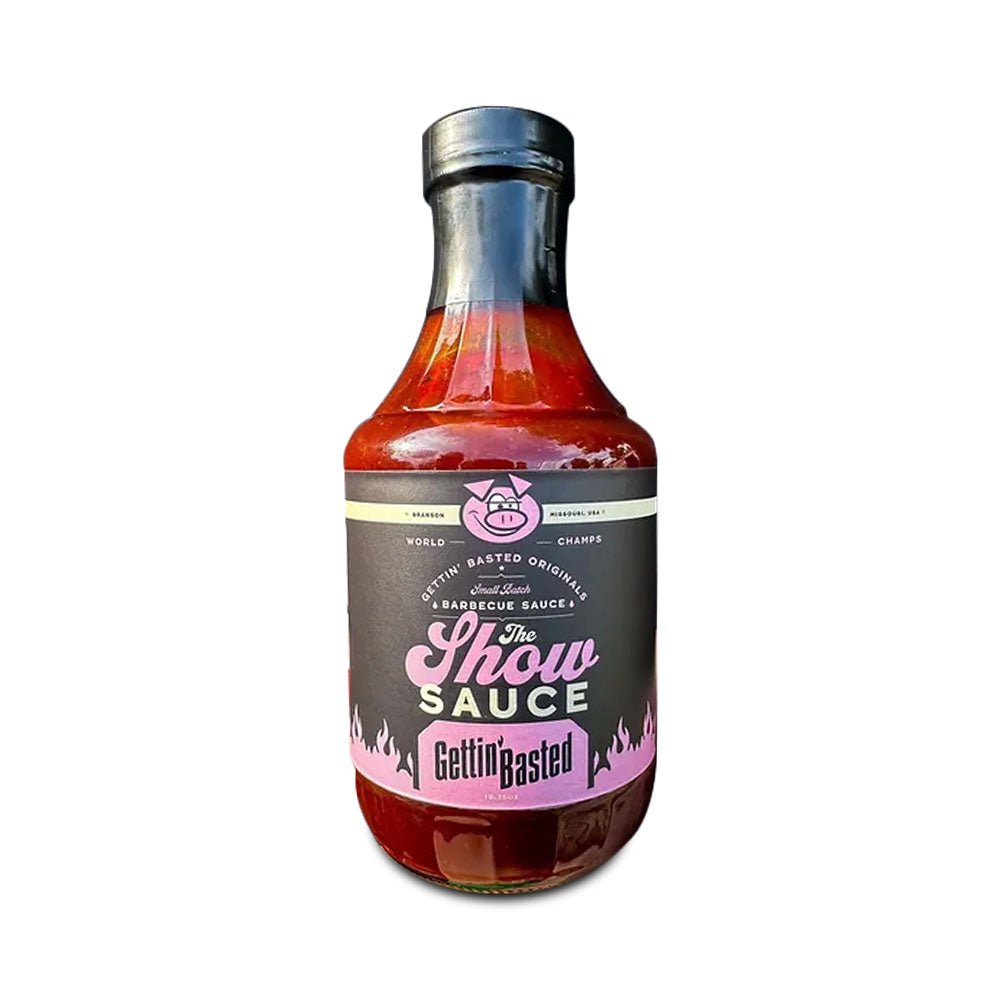 Bottle of Gettin’ Basted 'The Show' barbecue sauce with a black label featuring pink accents, including a small pig icon at the top, flames along the bottom, and bold text in the center. The label reads 'World Champs' and 'Missouri, USA,' indicating the brand's award-winning reputation.