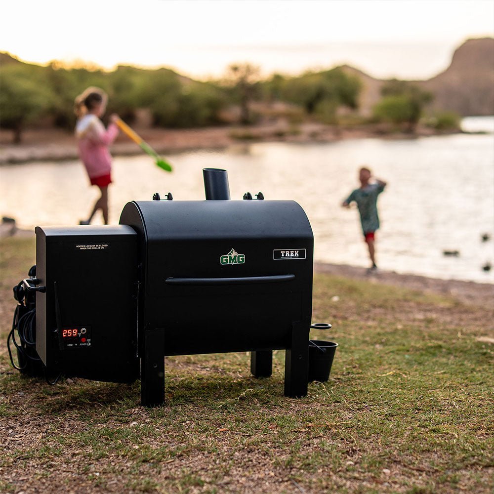 A grill on the shore of a lake with two children playing in the background and trees visible along the shore.