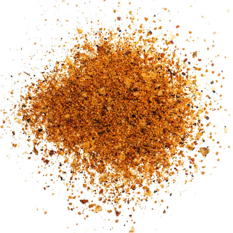 A close-up view of Heavy Smoke White Label Rub, showing a pile of the seasoning mix. The rub consists of various-sized granules in shades of brown, red, and black, indicating a blend of spices and seasonings.