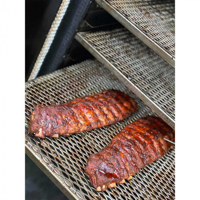 Two racks of barbecued ribs on mesh grates inside a BBQ smoker, showing the ribs cooked to a deep, rich brown color.