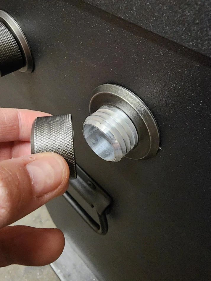 Close-up of a hand holding a threaded metal cap next to its corresponding threaded port on the side of a BBQ smoker.