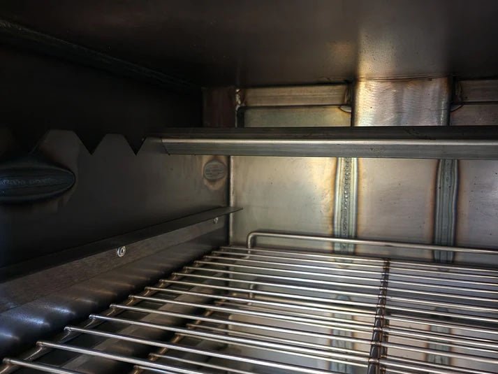 The interior of a BBQ smoker with a metal rack installed, highlighting the sturdy construction and notched brackets.