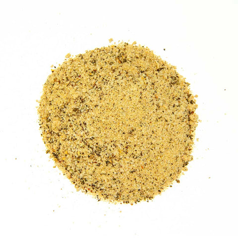 Close-up view of a coarse, golden-brown seasoning blend with visible spices and grains, spread out on a white surface.