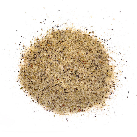 Close-up of a light beige seasoning blend with visible flakes of green and red spices, scattered on a white surface, suggesting a blend of citrus and spicy flavors.