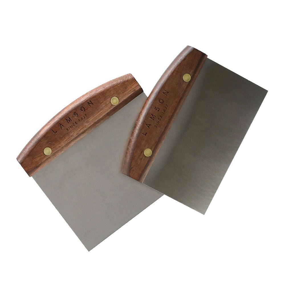 Two Lamson dough scrapers with stainless steel blades and wooden handles are crossed over each other against a white background. The handles feature brass rivets, and the Lamson logo is engraved on the wood.