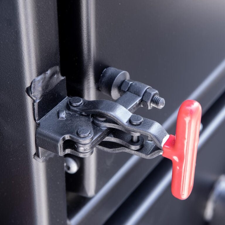 Close-up of the latch mechanism on the Meadow Creek BX25 smoker, featuring a red handle and a black metal latch assembly.