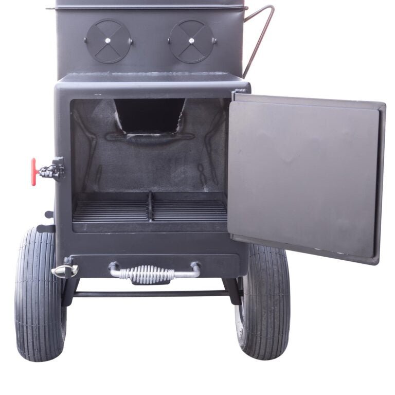 Front view of the open firebox of a Meadow Creek smoker, revealing the main cooking chamber with grates and the firebox below. The smoker has two large wheels for mobility and adjustable air vents on the door and side.