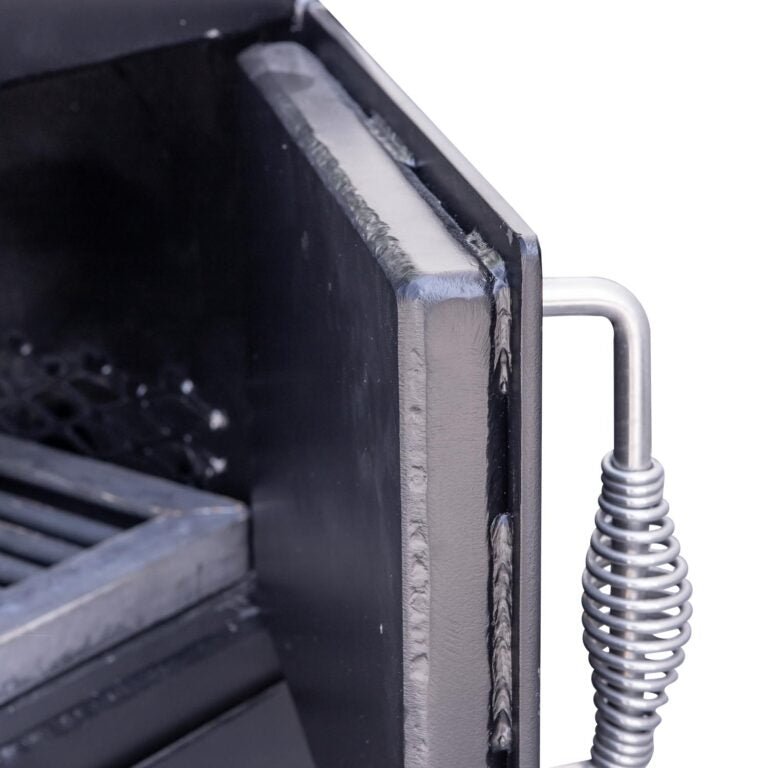 Close-up of the insulated firebox door on a BBQ smoker, showing the heavy-duty construction and hinge details