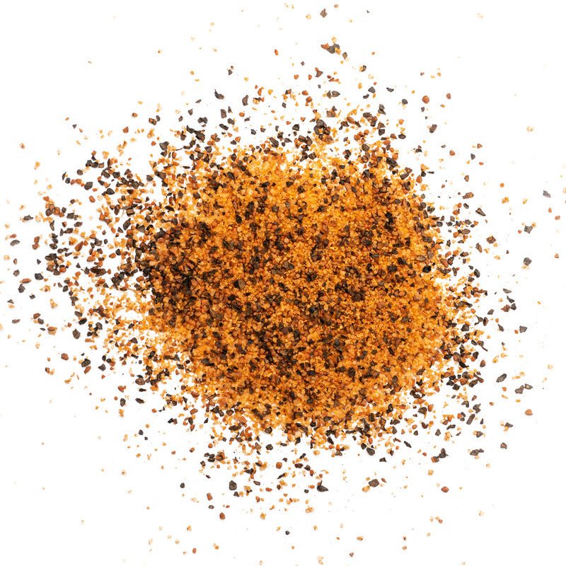 A close-up view of a pile of Meat Church Holy Cow BBQ Rub. The spice mix is a coarse, reddish-orange powder with visible black pepper flakes.