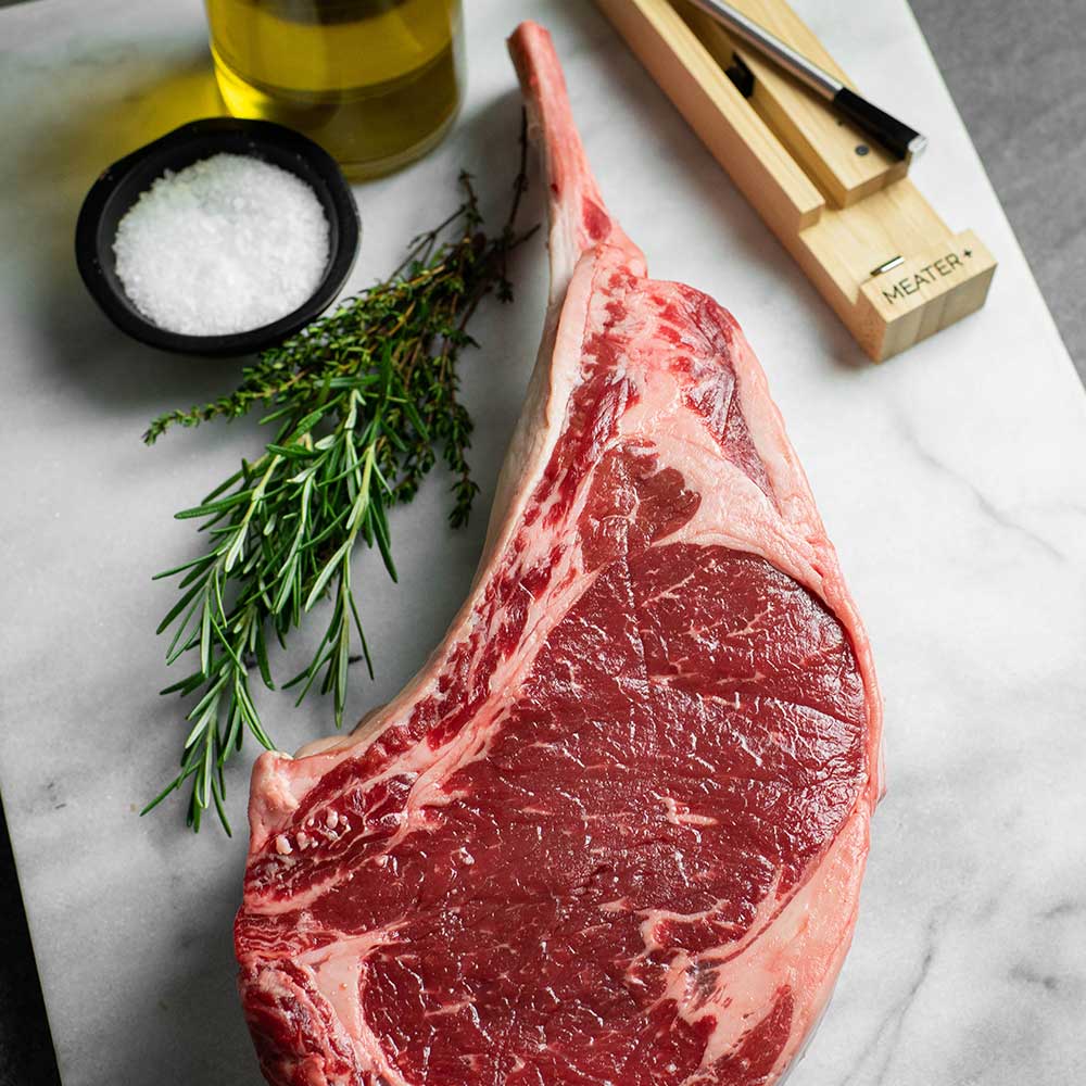 Photo of a steak on a cutting board with salt, oil and herbs, along with the probe.