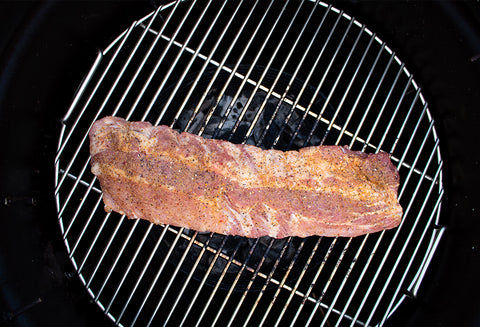 A raw, seasoned pork rib on a circular grill grate with visible spices and seasonings.