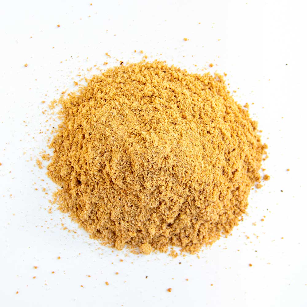 Close-up of a fine, tan-colored pork seasoning blend spread out on a white surface, showing a uniform texture with fine granules, indicating its blend for pork injections.