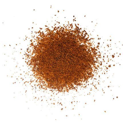 A close-up view of a pile of Simply Marvelous Santa Maria Rub spice blend, showing its coarse, reddish-brown granules scattered on a white surface.