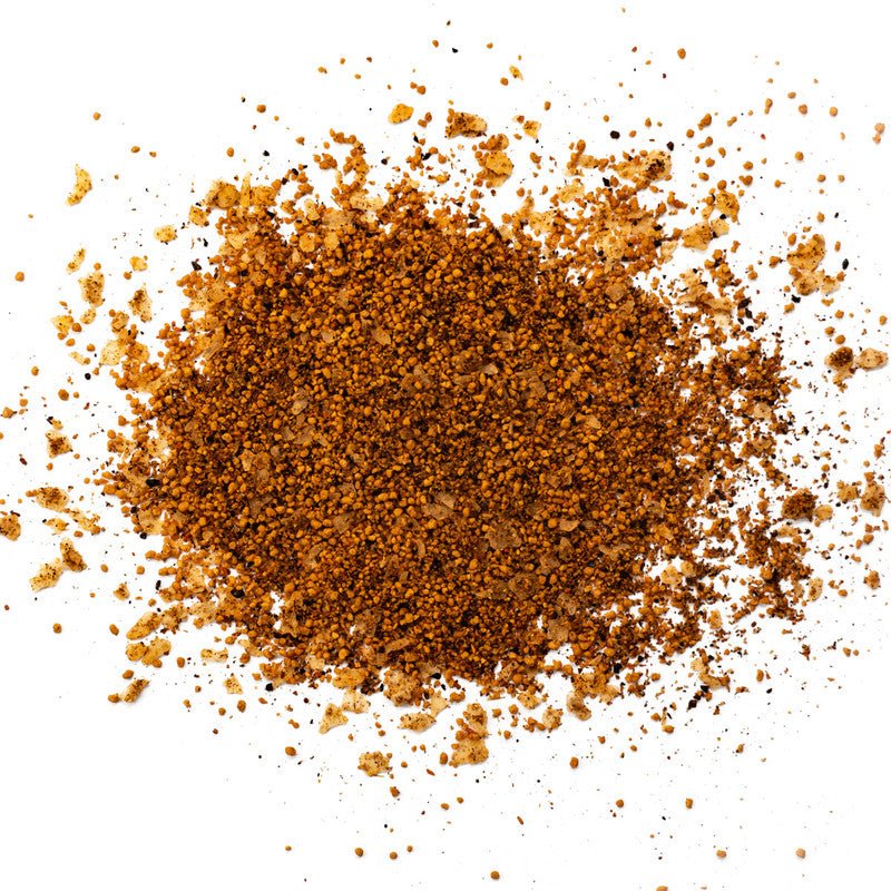 A close-up image of Simply Marvelous Spicy Apple rub. The seasoning consists of a mix of brown and beige coarse spices spread out on a white surface.