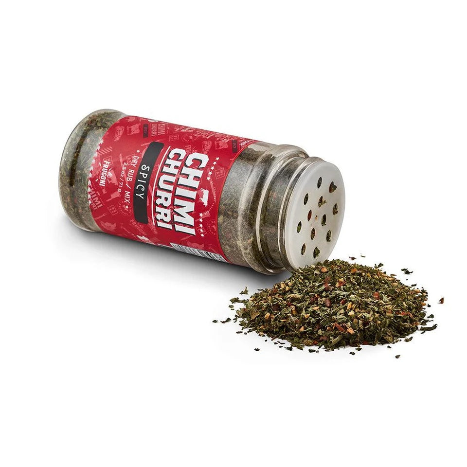 A jar labeled 'CHIMI CHURRI Spicy Dry Rub / Mix' is tipped over, spilling its contents of mixed herbs and spices onto a white surface.