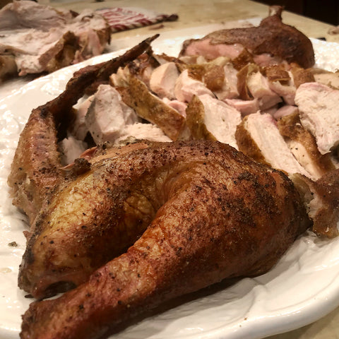 A cooked whole turkey with golden-brown, crispy skin served on a white platter, surrounded by slices of similarly prepared turkey, showcasing a succulent and seasoned exterior.